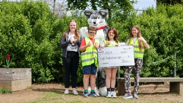 Student holding a large cheq with Husky mascot and local SPCA representative