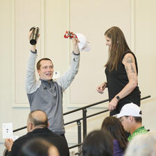 Man with his arms raised holding prizes he received from the woman standing on stage